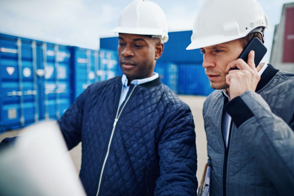 Engineers discussing building plans while standing in a container yard